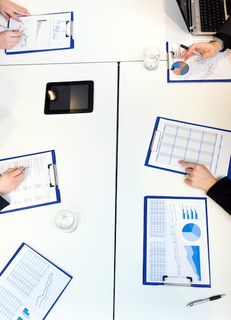 A detailed, high-angle shot of budget documents and financial reports laid out on a conference table, with people in the background engaged in discussion, symbolizing the intensive scrutiny and debate involved in defense budget analysis.