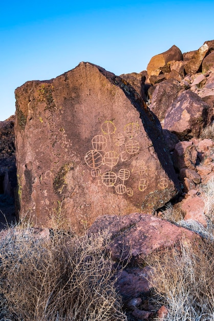 A detailed photo of intricate petroglyphs on a rock face in the US Southwest, with subtle signs of erosion around them and a background of parched, cracked earth, symbolizing the impact of climate extremes on ancient art.